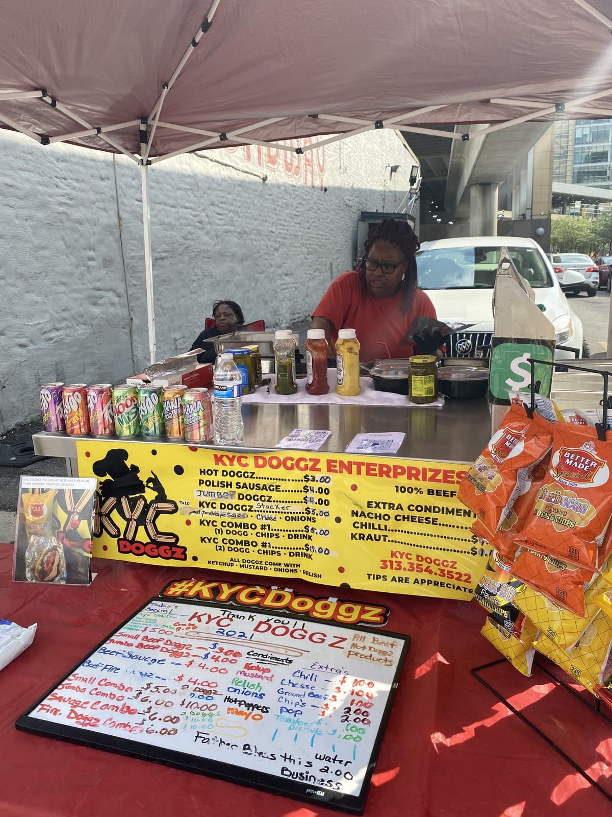 Karen at the full KYC Doggz Enterprizes setup with signage and menu boards downtown